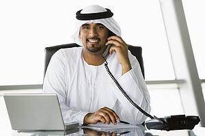 Businessman in office with laptop on telephone smiling (high key/selective focus)