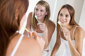 Two women in bathroom brushing teeth and smiling