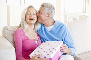 Husband giving wife gift in living room kissing her and smiling