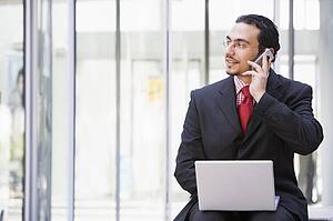 Businessman sitting outdoors by building with a laptop on cellular phone (high key/selective focus)