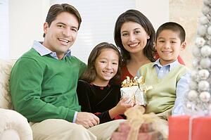Family Sitting On Sofa Together, Holding A Christmas Gift