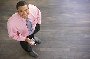 Businessman standing indoors with cellular phone smiling