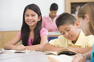 Students in class reading with teacher in background (selective focus)