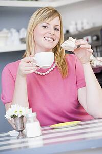 Young woman sitting at a table drinking tea and eating a sweet treat