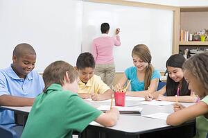 Students in class writing with teacher at front board