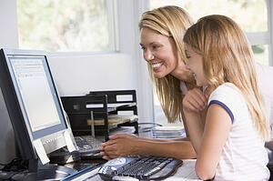 Woman and young girl in home office with computer smiling