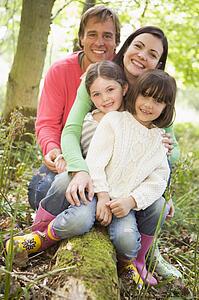 Family outdoors in woods sitting on log smiling