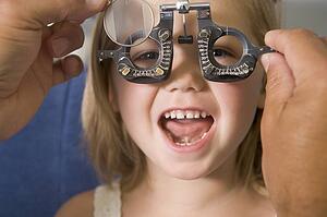 Optometrist in exam room with young girl in chair smiling