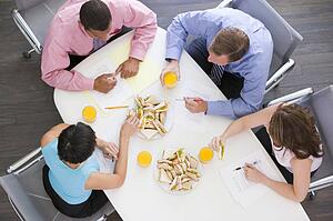 Four businesspeople at boardroom table with sandwiches