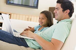 Man with young girl in living room with laptop smiling