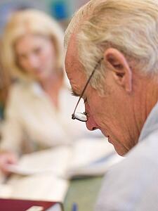 Man in library reading with woman in background (selective focus)
