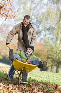 Man and young boy outdoors playing with wheelbarrow and smiling (selective focus)