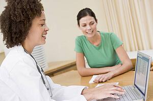 Doctor using laptop with woman in doctor's office smiling
