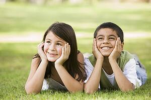 Two young children outdoors lying in park smiling (selective focus)