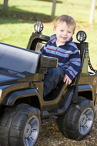 Young boy playing outdoors in toy truck smiling
