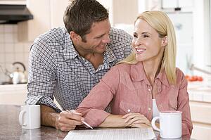 Couple in kitchen with newspaper and coffee smiling
