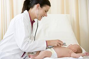 Doctor giving checkup with stethoscope to baby in exam room smiling