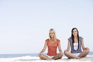 Two women sitting and meditating on a beach