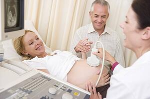 Pregnant woman getting ultrasound from doctor with husband watching
