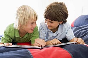 Two Young Boys Lying Down On A Bed Reading A Book