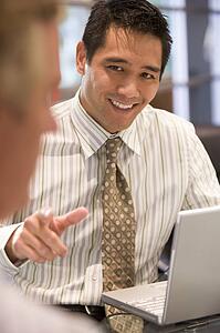 Two businessmen in boardroom with laptop talking