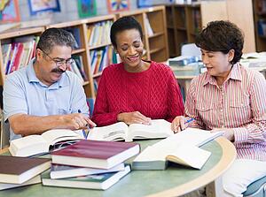 Three people sitting in library with books and notepads (selective focus)