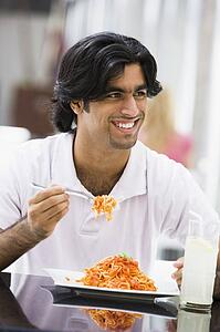 Man at restaurant eating spaghetti and smiling (selective focus)