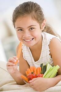 Young girl eating bowl of vegetables in living room smiling