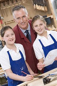Female students reviewing woodworking plans with teacher
