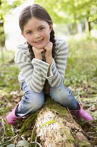 Young girl outdoors in woods sitting on log smiling