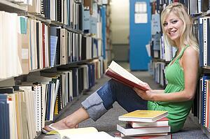 Woman sitting on floor in library holding book