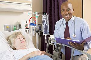 Doctor Making Notes About Senior Woman Lying In Hospital Bed