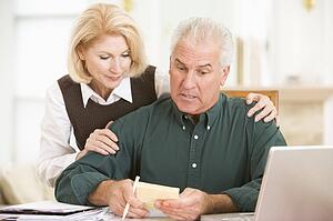 Couple in dining room with laptop and paperwork looking worried
