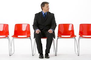 Businessman Sitting In Row Of Empty Chairs 