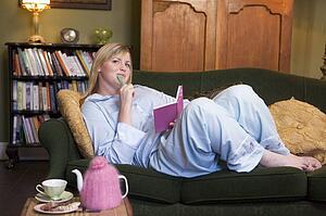 Young woman lying on sofa at home writing in her diary