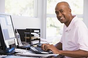 Man in home office using computer and smiling