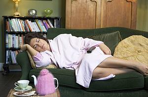 Young woman lying on sofa falling asleep while watching television