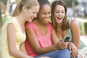 Teenage Girls Sitting Outside Playing With Mobile Phone