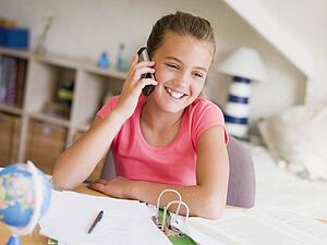 Young Girl Distracted From Her Homework, Talking On A Cellphone