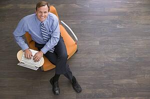 Businessman sitting indoors with laptop smiling