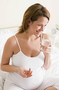 Pregnant woman in bedroom holding medicine and water smiling