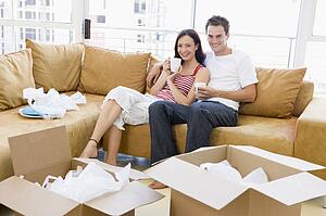 Couple relaxing with coffee by boxes in new home smiling