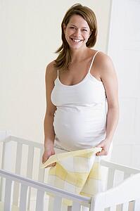 Pregnant woman setting up baby crib smiling