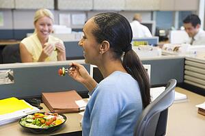 Businesswoman in cubicle eating salad and smiling