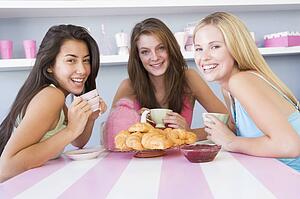 Three young woman sitting at a table having tea and a snack