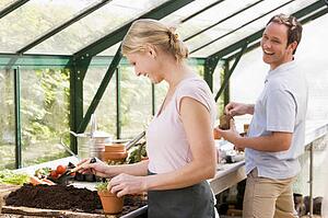 Couple in greenhouse putting soil in pots smiling