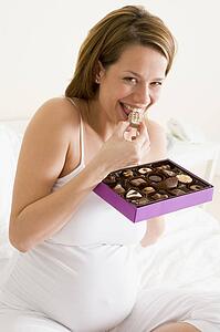 Pregnant woman in bed eating chocolate smiling