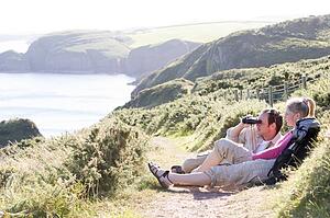 Couple on cliffside outdoors using binoculars and smiling