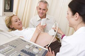 Pregnant woman getting ultrasound from doctor with husband looking at picture