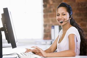Businesswoman in office wearing headset and typing on computer smiling